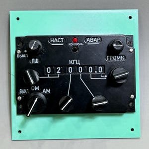 以下が含まれることがあります： 「02000.0」と表示されたデジタルディスプレイを持つ黒いコントロールパネル。パネルには、キリル文字で「HAСТ」、「АВАР」、「ГРОМК」、「ВЫКЛ」、「ПШ」、「ОМ」、「АМ」など、いくつかのノブとスイッチがあります。