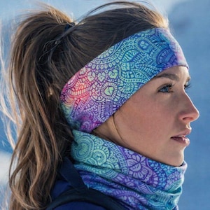 Op de afbeelding: Een kleurrijke hoofdband en nekwarmer set. De hoofdband en nekwarmer hebben een gedetailleerd, herhalend patroon in tinten blauw, paars en roze. Het ontwerp doet denken aan een mandala of ingewikkeld kant. De set is waarschijnlijk gemaakt van een zacht, rekbaar materiaal.