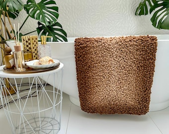 May include: A brown and beige bath mat with a textured, fluffy surface. The mat is made of a soft, absorbent material and is perfect for adding a touch of style to any bathroom.