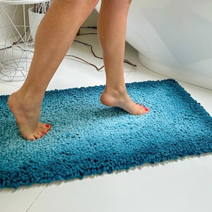 Op de afbeelding: Een blauwe en turquoise badmat met een verloop. De mat is gemaakt van zachte, pluche vezels en is perfect om water op te nemen na het douchen.