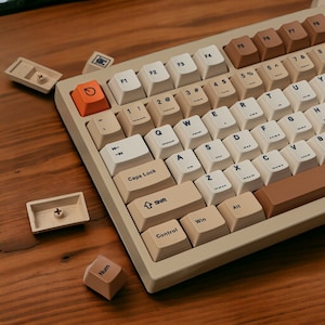May include: A beige and brown mechanical keyboard with a variety of keys, including function keys, number keys, letter keys, and arrow keys. The keyboard has a beige and brown color scheme with a light brown frame and beige keys. The keys have black lettering and symbols.