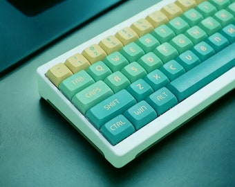 May include: A white and green keyboard with a light yellow top row. The keys are labeled with letters and symbols. The keyboard is on a green surface.