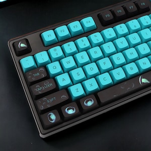 May include: A black mechanical keyboard with teal keycaps and a dark brown frame. The keyboard has a standard layout with function keys, number keys, and letter keys. The keycaps have a unique design with a subtle pattern.