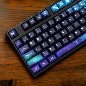 May include: A black mechanical keyboard with a space bar featuring a galaxy design. The keys are labeled with the standard alphabet and number keys. The keyboard has a blue and purple color scheme.