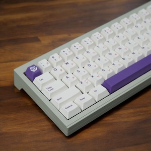 May include: A white mechanical keyboard with a purple accent bar and Japanese keycaps. The keyboard has a light gray case and a rose-shaped keycap.