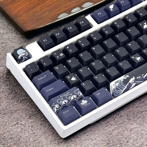 May include: A white mechanical keyboard with black keys and blue and white keycaps featuring a wave design. The keyboard has a white frame and a black and white wave design on the bottom right corner.