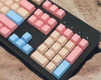 May include: A black keyboard with a variety of pastel pink and cream colored keys. The keyboard has a number pad and arrow keys. The keys are labeled with letters, numbers, and symbols.