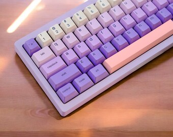 May include: A purple and cream keyboard with a pink space bar. The keyboard has a variety of keys, including letters, numbers, and symbols.