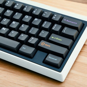 May include: A black and white mechanical keyboard with a white frame. The keyboard has a standard layout with keys labeled with letters, numbers, and symbols. The keys are black with white lettering. The keyboard has a white frame and is sitting on a wooden surface.