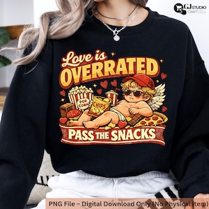 May include: Black sweatshirt with a graphic featuring a cartoon cupid wearing sunglasses and a red cap, surrounded by snacks. Text reads "Love is OVERRATED" and "PASS THE SNACKS". Hearts and stars decorate the design.
