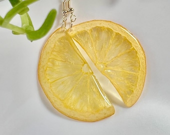 May include: A pair of lemon slice earrings with gold-toned hooks. The earrings are made of resin and feature a realistic depiction of a lemon slice.