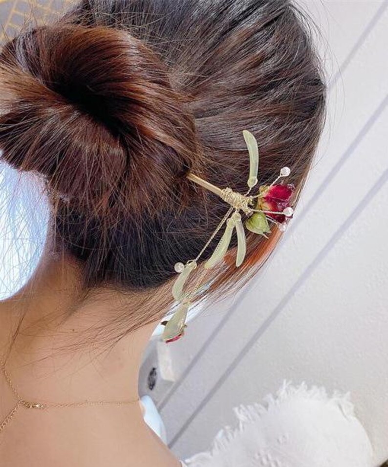 May include: A gold hair stick with a red and green flower design. The stick is decorated with small beads and has a long, thin stem.