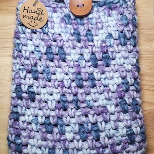 May include: A crocheted phone case in shades of purple, blue, and white with a wooden button and a brown tag that says "Hand made" with a smiley face.