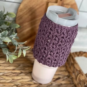 May include: Purple crocheted cup cozy with a white lid on a woven tray.