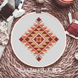 May include: A cross-stitch pattern with a geometric design in shades of orange, red, and yellow. The pattern is stitched on white Aida cloth and framed in a wooden hoop.