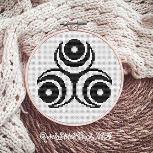 Puede incluir: Un patrón de punto de cruz en blanco y negro de un diseño de triple espiral estilizado, enmarcado en un aro de bordado de madera.