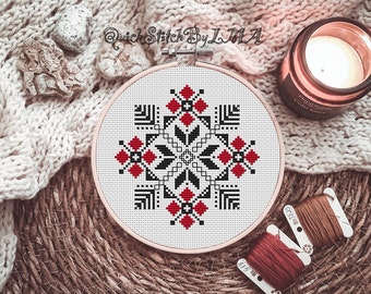 May include: A white embroidery hoop with a black and red geometric pattern. The hoop is on a woven surface with a candle and yarn.