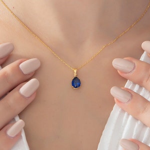 Könnte beinhalten: Eine goldene Kettenkette mit einem tropfenförmigen Anhänger mit einem dunkelblauen Edelstein.