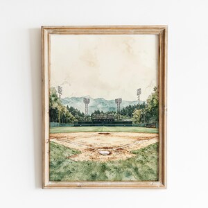 Pode incluir: Pintura em aquarela de um campo de beisebol em uma moldura de madeira. O campo &eacute; cercado por &aacute;rvores e montanhas ao fundo. O c&eacute;u &eacute; de cor bege claro. A pintura tem um toque vintage.