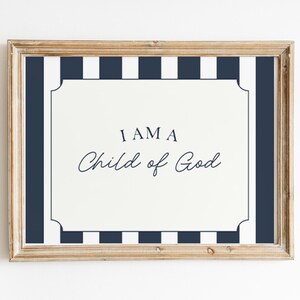 Pode incluir: Uma impress&atilde;o emoldurada com o texto "I AM A Child of God" em uma fonte decorativa. A impress&atilde;o tem um fundo branco com uma borda listrada azul marinho e branca e uma moldura dourada.
