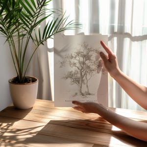 Puede incluir: Un dibujo en blanco y negro de un &aacute;rbol sobre un fondo blanco. El dibujo est&aacute; enmarcado y sostenido por las manos de una persona. El texto "Rooted in Love, Ephesians 3:17" est&aacute; impreso debajo del dibujo.
