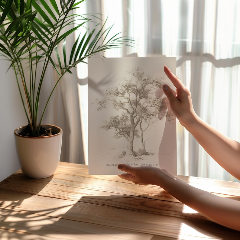 Puede incluir: Un dibujo en blanco y negro de un &aacute;rbol sobre un fondo blanco. El dibujo est&aacute; enmarcado y sostenido por las manos de una persona. El texto "Rooted in Love, Ephesians 3:17" est&aacute; impreso debajo del dibujo.