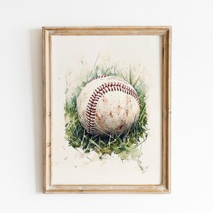 Pode incluir: Pintura em aquarela de uma bola de beisebol na grama verde. A bola &eacute; esbranqui&ccedil;ada com costuras vermelhas e mostra sinais de desgaste. A obra de arte &eacute; emoldurada em uma moldura de madeira clara, ideal para f&atilde;s de esportes.