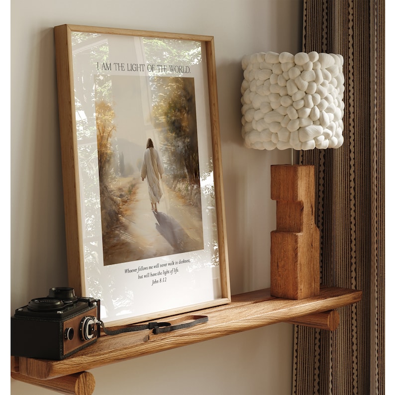 Puede incluir: Una impresi&oacute;n enmarcada con el texto "I AM THE LIGHT OF THE WORLD" y una representaci&oacute;n de una persona caminando por un camino. Una l&aacute;mpara de madera y una c&aacute;mara vintage est&aacute;n sobre una estanter&iacute;a de madera.