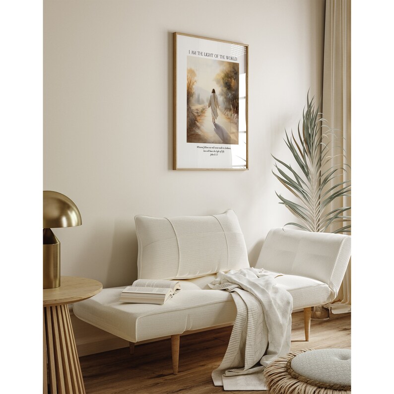 Puede incluir: Un cuadro enmarcado con el texto "I AM THE LIGHT OF THE WORLD" cuelga sobre una chaise longue color crema. La impresi&oacute;n representa una figura caminando por un camino. Una l&aacute;mpara dorada y una peque&ntilde;a mesa de madera est&aacute;n a la izquierda.