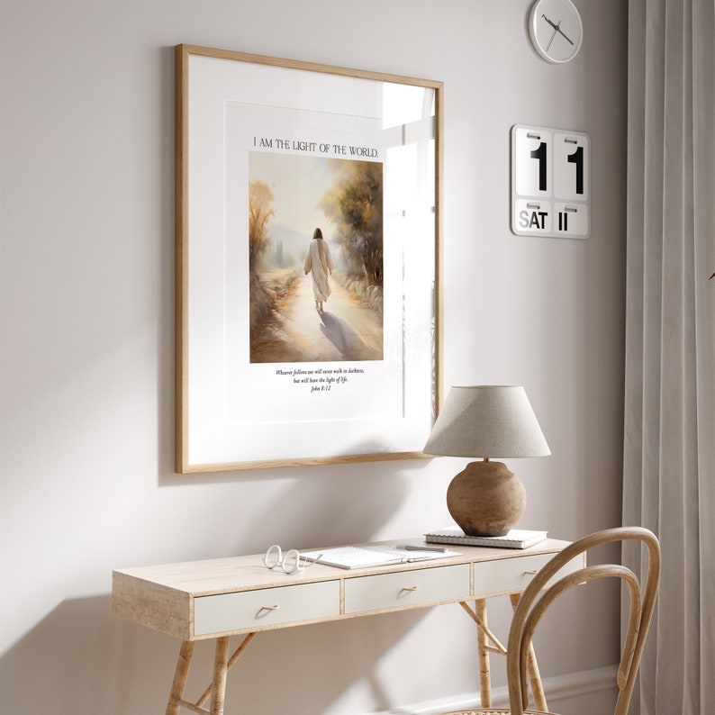 Puede incluir: Impresi&oacute;n art&iacute;stica enmarcada con el texto &laquo;I AM THE LIGHT OF THE WORLD&raquo; sobre una imagen de una figura caminando por un camino. La impresi&oacute;n est&aacute; en un marco de madera y cuelga sobre un escritorio con una l&aacute;mpara y un calendario.