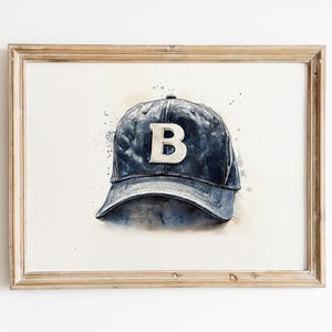 Pode incluir: Pintura em aquarela de um bon&eacute; de beisebol azul com um "B" branco na frente. A obra de arte &eacute; emoldurada em uma moldura de madeira clara. O fundo tem respingos de aquarela azul.