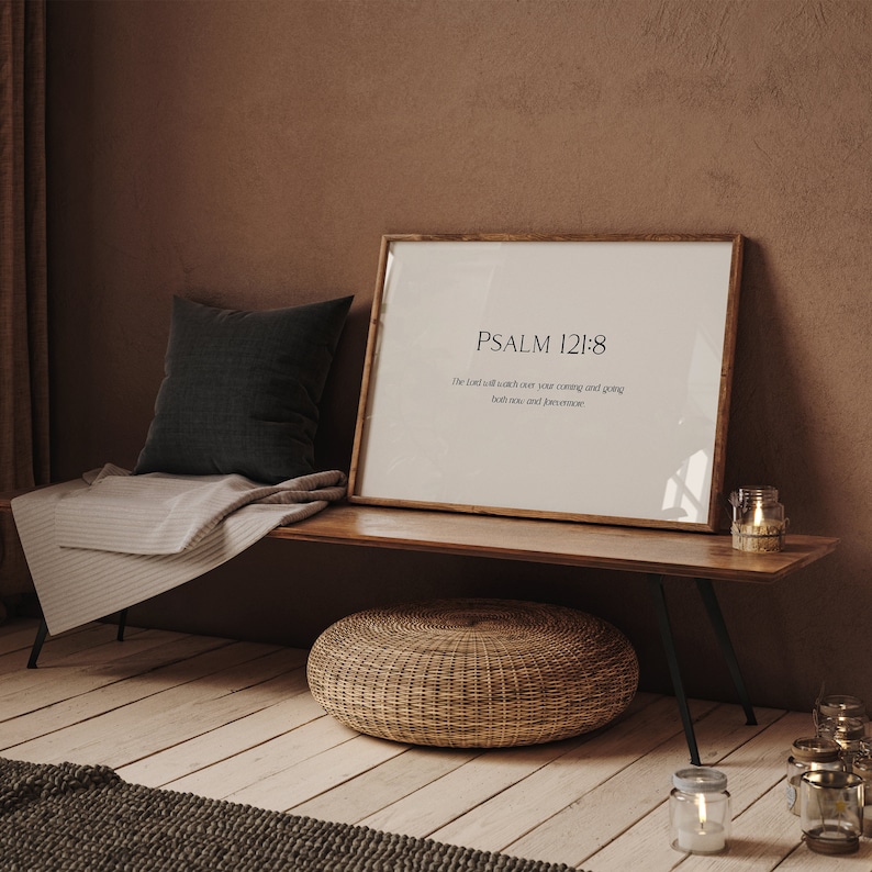 May include: A framed print with a white background and black text that reads "PSALM 121:8" and "The Lord will watch over your coming and going both now and forevermore". The print is on a wooden shelf with a woven basket and candles.