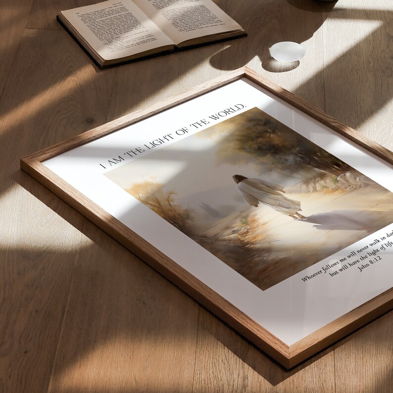 Puede incluir: Impresi&oacute;n art&iacute;stica enmarcada con tem&aacute;tica religiosa. La obra representa una figura con t&uacute;nica blanca caminando hacia una luz brillante. El texto "I AM THE LIGHT OF THE WORLD" est&aacute; en la parte superior, con un vers&iacute;culo b&iacute;blico en la parte inferior. El marco es de madera clara.
