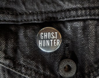 Könnte beinhalten: Ein schwarz-weißer Knopf mit dem Text "Ghost Hunter" auf einer schwarzen Jeansjacke.