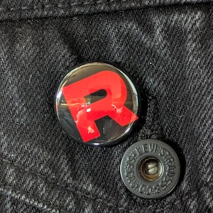 May include: Close-up of a black denim jacket with a red "R" button and a black button with the text "LEVI STRAUSS & CO." The buttons are set against the textured denim fabric.