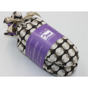Könnte beinhalten: Ein zylindrisches Paket, das in Stoff mit einem schwarz-weißen Polka-Dot-Muster verpackt ist. Ein lila Etikett mit dem Text "LILLAS LAVENDER" ist um die Mitte gewickelt. Das Paket ist mit einem beigen Band gebunden.