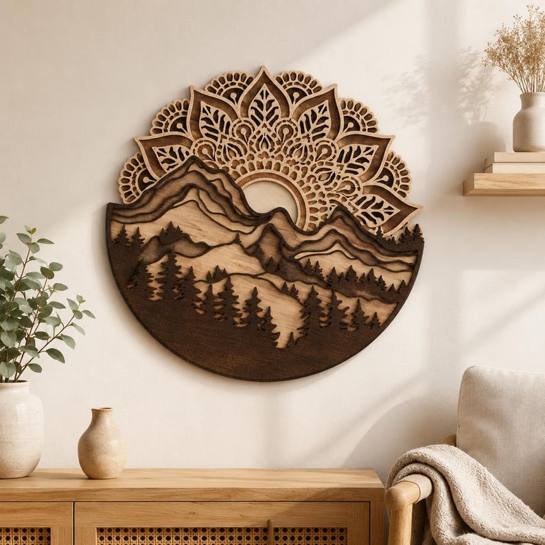 May include: A circular wall art piece crafted from layered wood, featuring a detailed mountain range and forest silhouette at the bottom, topped with an intricate, symmetrical mandala pattern in varying shades of brown and natural wood tones.