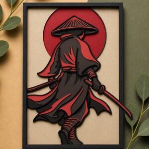 May include: Framed paper art of a samurai in black and red. The figure is viewed from behind, wearing a traditional hat and holding two swords. A red sun is in the background. The artwork is presented in a black frame.