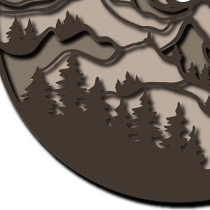 May include: A circular wall art piece featuring a layered, cut-out design of a mountain range and a dense forest of pine trees. The artwork uses varying shades of brown and beige to create depth, with dark brown silhouettes of trees in the foreground.