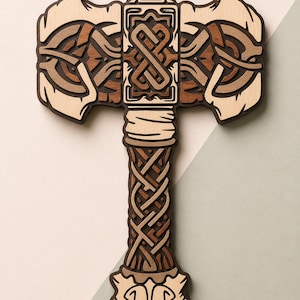 Può includere: Un'applique da parete in legno a forma di martello. La testa del martello presenta intricati disegni a strati nei toni del marrone e del beige. L'impugnatura è un motivo intrecciato dettagliato. Il design ricorda l'arte vichinga o norrena.