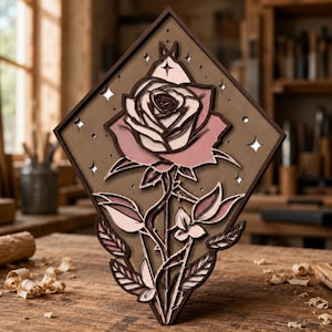May include: A layered wooden art piece featuring a rose design. The rose is pink and white, set against a brown background within a diamond-shaped frame. The piece includes star cutouts and is displayed on a wooden surface.