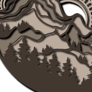 May include: A circular multi-layered wall art piece featuring a mountain range and a forest of pine trees in shades of dark brown, light brown, and beige. The design includes intricate cutouts and a sun motif with a decorative mandala pattern.