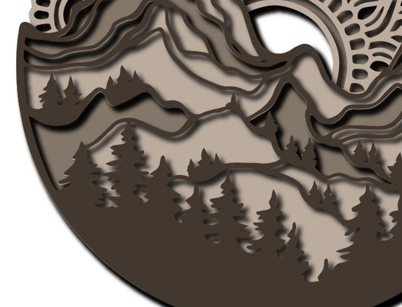 May include: A circular multi-layered wall art piece featuring a mountain range and a forest of pine trees in shades of dark brown, light brown, and beige. The design includes intricate cutouts and a sun motif with a decorative mandala pattern.