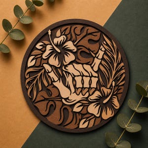 May include: A round wooden wall art piece featuring a skeleton hand giving the shaka sign, surrounded by hibiscus flowers and tropical leaves. The artwork is made of layered wood in shades of brown and tan.