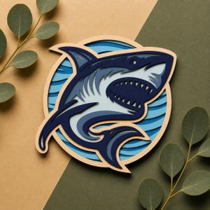 Peut inclure: Un design de requin en bois multicouche dans les tons de bleu et de blanc, sur un fond marron clair et vert. Le requin est à l'intérieur d'un cercle bleu et blanc, avec une bouche ouverte détaillée. Des feuilles d'eucalyptus sont dans les coins.