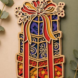 May include: A layered wooden gift box design with a red, yellow, and blue color scheme. The top features a bow and floral accents. The design includes intricate cut-out patterns and star shapes.
