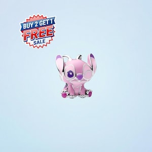 May include: A pink enamel charm featuring the character Angel from Lilo & Stitch. The charm has a silver-colored bail and is winking. The charm is set against a light blue background. A "BUY 2 GET 1 FREE SALE" sticker is in the upper left corner.