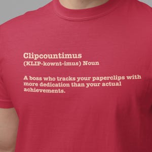 Pode incluir: Camiseta vermelha com a definição branca de "Clipcountimus". A definição descreve com humor um chefe obcecado por clipes de papel. A camiseta também inclui a pronúncia da palavra.
