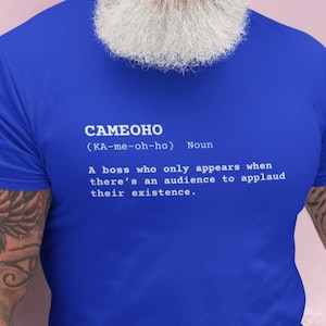 Pode incluir: Uma camiseta azul com a palavra "CAMEOHO" em letras brancas. Abaixo, a pronúncia fonética e a palavra "Substantivo". O texto descreve um chefe que só aparece quando há uma audiência.