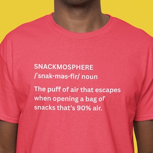 May include: A red t-shirt with the word "SNACKMOSPHERE" and its phonetic pronunciation in white text. Below, a definition describes the puff of air escaping a snack bag, which is 90% air.